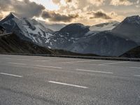 a mountain landscape showing a car parked on an empty parking lot next to snow covered mountains