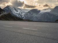 a mountain landscape showing a car parked on an empty parking lot next to snow covered mountains