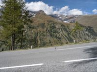 a motorcycle rider riding the road with a mountain in the background in europe and a sign in the foreground