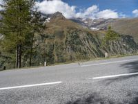 a motorcycle rider riding the road with a mountain in the background in europe and a sign in the foreground