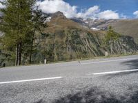 a motorcycle rider riding the road with a mountain in the background in europe and a sign in the foreground