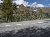 a motorcycle rider riding the road with a mountain in the background in europe and a sign in the foreground