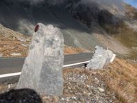 a road surrounded by tall rocks on a hillside with snow capped mountains behind it and a red traffic marker on the side