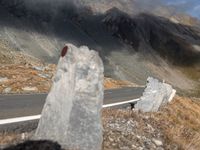 a road surrounded by tall rocks on a hillside with snow capped mountains behind it and a red traffic marker on the side