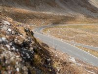 a long narrow mountain road through the grass covered hills above the road is a man riding on a motorcycle