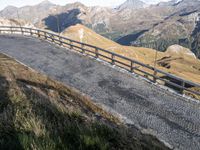 a paved road on the side of mountains next to grass and rocks on a cliff