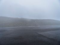 a stop sign is in a foggy, empty parking lot near a mountain road