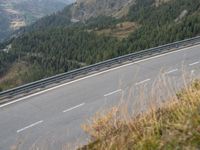 a man riding a bicycle on the road next to a forest in the mountains in a hilly area