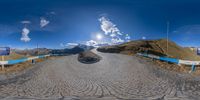 a wide angle 360 - view of a narrow road in the mountains with a mountain behind it