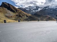 the motorcyclist is riding down a winding road surrounded by mountains, and snow capped peaks