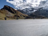 the motorcyclist is riding down a winding road surrounded by mountains, and snow capped peaks