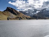 the motorcyclist is riding down a winding road surrounded by mountains, and snow capped peaks