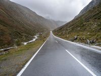 the mountain road leads to the side of a mountainside in the rain, with some water pouring on the side and a cloudy sky