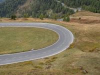 the road is curved and curving through the hills on a hill side slope in the distance are several trees