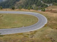 the road is curved and curving through the hills on a hill side slope in the distance are several trees