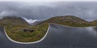 a couple of curved curves on a mountain road between mountains with clouds rolling in the background