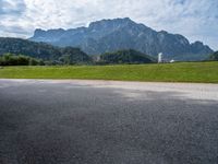 an empty road by a farm near the mountains with a clock tower in the distance