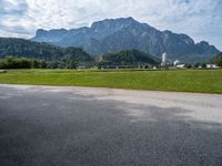 an empty road by a farm near the mountains with a clock tower in the distance