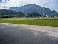 an empty road by a farm near the mountains with a clock tower in the distance