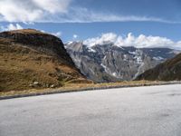 a person on a motor bike riding down the mountain path near a winding road with snow capped mountains in the background