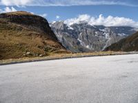 a person on a motor bike riding down the mountain path near a winding road with snow capped mountains in the background