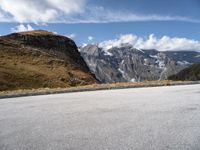 a person on a motor bike riding down the mountain path near a winding road with snow capped mountains in the background