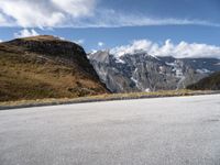 a person on a motor bike riding down the mountain path near a winding road with snow capped mountains in the background