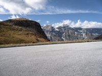 a person on a motor bike riding down the mountain path near a winding road with snow capped mountains in the background