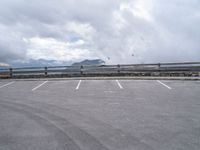 an empty parking lot in a mountain with mountains behind it and clouds on the top of the mountain