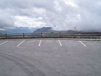 an empty parking lot in a mountain with mountains behind it and clouds on the top of the mountain