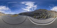 a 360 - view image of an asphalt road through some rocks and bushes with clouds