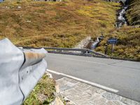 view of road in front of rock outcropping with stream flowing down the hill