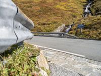 view of road in front of rock outcropping with stream flowing down the hill