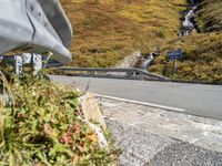 view of road in front of rock outcropping with stream flowing down the hill