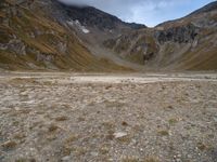 the small white car is parked in the mountains with the rocky side and grass below