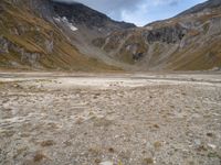 the small white car is parked in the mountains with the rocky side and grass below