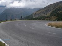 there is a small motorcycle that is on the road near mountains and clouds as well