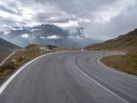 an empty road is winding into the mountains on a cloudy day with clouds flying overhead