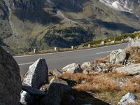 a person is riding their motorcycle down the side of a mountain road in front of a large boulder