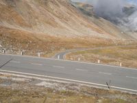 a motorcycle is parked on a mountain road on a cloudy day with smoke rising from the distance
