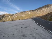 the curved road goes along the side of the mountain range of mountains with snow and clouds above