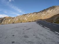 the curved road goes along the side of the mountain range of mountains with snow and clouds above