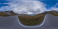 a panoramic image of two curved roads on a grassy field and mountains in the background