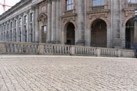 a large old building with columns and arched pillars is in the center of a cobblestone street