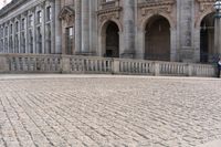 a large old building with columns and arched pillars is in the center of a cobblestone street