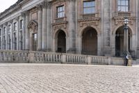 a large old building with columns and arched pillars is in the center of a cobblestone street