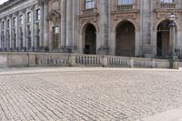 a large old building with columns and arched pillars is in the center of a cobblestone street