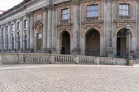 a large old building with columns and arched pillars is in the center of a cobblestone street