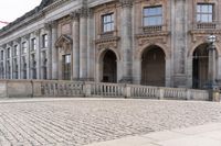 a large old building with columns and arched pillars is in the center of a cobblestone street