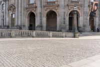 a large old building with columns and arched pillars is in the center of a cobblestone street